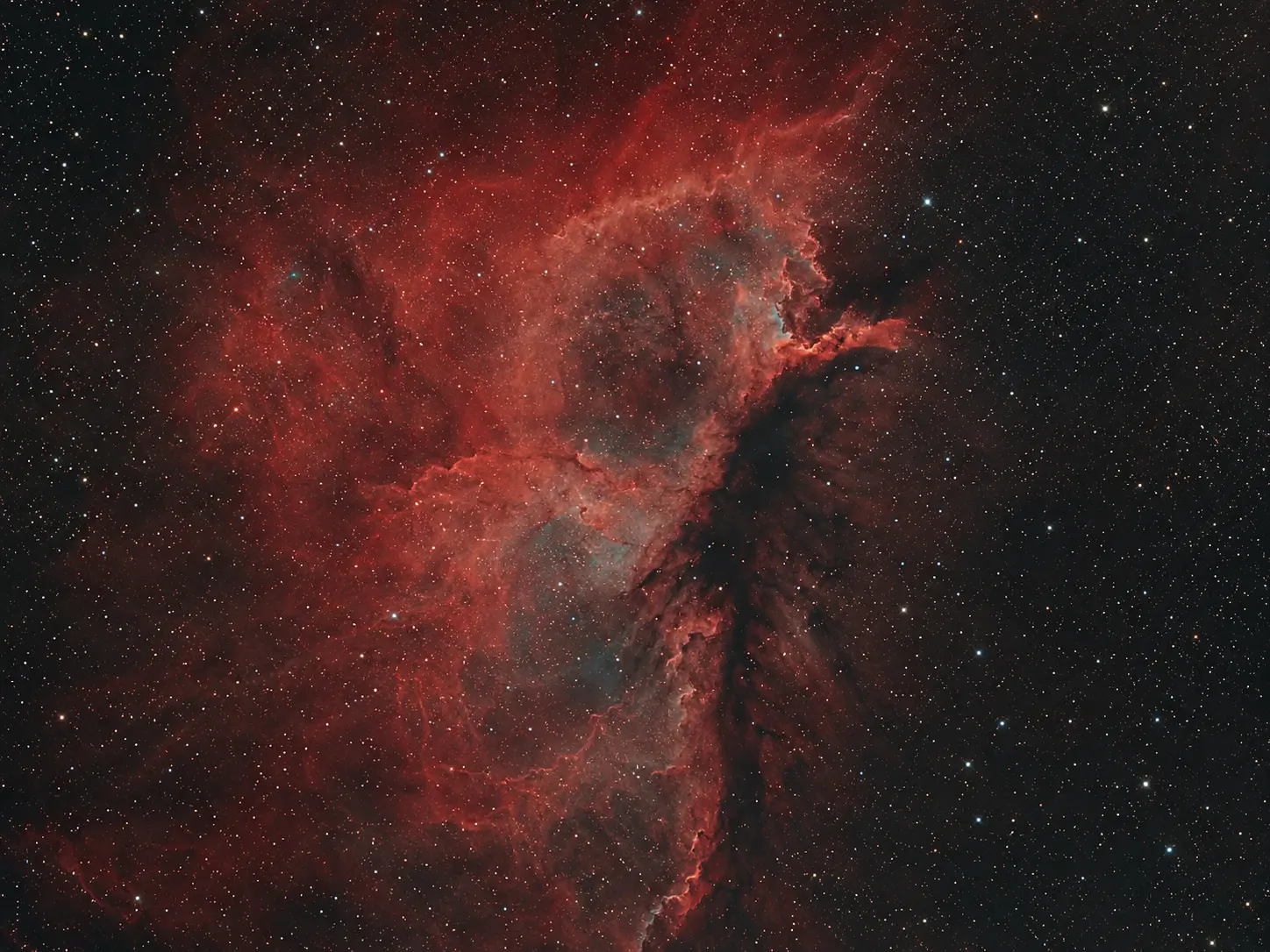 The Pelican Nebula glowing red among dark dust